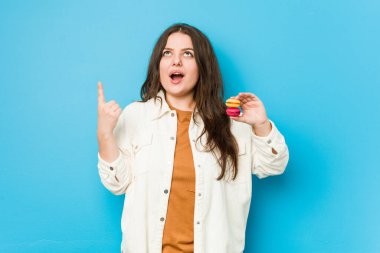 Genç, kıvrımlı bir kadın, elinde açtığı ağızla baş aşağı duran badem kurabiyeleri tutuyor..