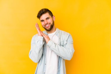 Sarı arka planda izole edilmiş genç beyaz adam enerjik ve rahat hissediyor, ellerini ovuşturuyor kendinden emin..
