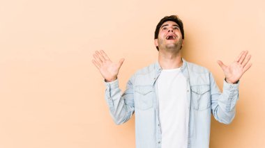 Bej arka planda izole edilmiş genç adam gökyüzüne haykırıyor, yukarı bakıyor, hayal kırıklığına uğramış..