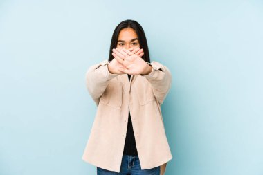 Mavi arka planda izole edilmiş genç bir kadın inkar jesti yapıyor.