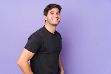 Mor arka planda izole edilmiş genç bir adam. Kendine güveniyor. Ellerini kalçasında tutuyor..