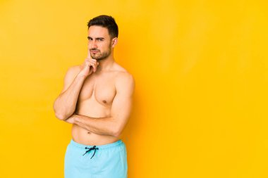 Sarı arka planda mayosu olan genç, beyaz bir adam. Kafkasyalı genç, tefekkür eden, bir strateji planlayan, bir iş adamı..