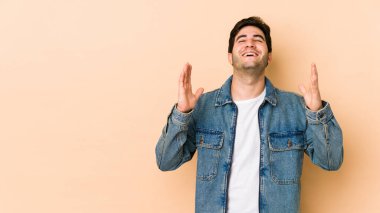 Bej arka planda izole olmuş genç adam kahkahalar atıyor elini göğsüne koyuyor..