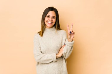 Bej arka planda izole edilmiş genç bir kadın iki numarayı parmaklarıyla gösteriyor..