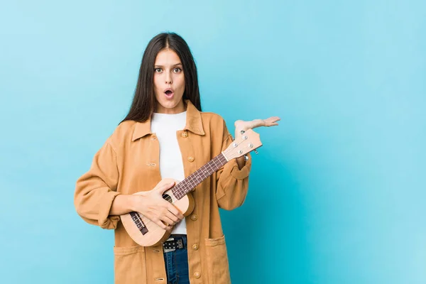 Junge Kaukasierin Mit Ukelele Beeindruckt Mit Kopierraum Auf Handfläche — Stockfoto