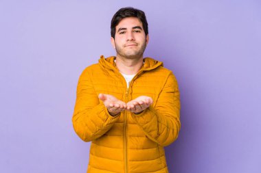 Mor arka planda izole edilmiş genç bir adam elinde avuç içi bir şeyle kameraya sunuyor..