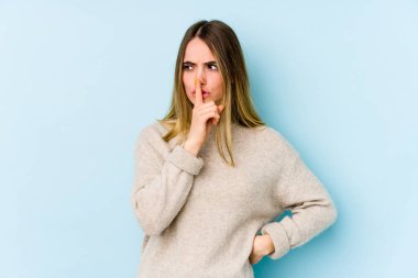 Mavi arka planda izole edilmiş genç beyaz kadın ya sır saklıyor ya da sessizlik istiyor..