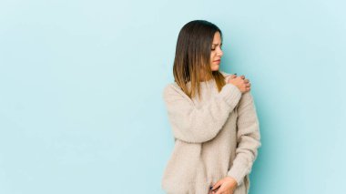 Mavi arka planda, omuz ağrısı çeken genç bir kadın..