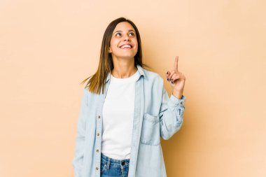 Bej arka planda izole edilmiş genç bir kadın iki ön parmağı da boş bir alan gösteriyor..