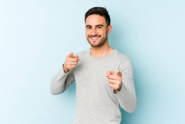 Mavi arka planda izole edilmiş genç beyaz adam parmaklarıyla ön tarafı işaret ediyor..