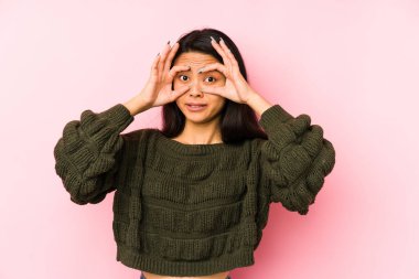 Pembe arka planda izole edilmiş genç Çinli kadın başarı fırsatı bulmak için gözlerini açık tutuyor..