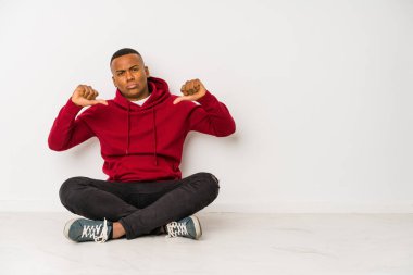 Yerde tek başına oturan genç latin adam gururlu ve kendinden emin, örnek olarak..