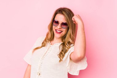 Pembe arka planda gözlüklü, tasasız ve heyecanlı genç beyaz bir kadın. Zafer konsepti.