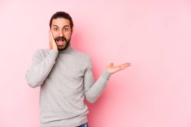 Pembe arka planda izole edilmiş genç, uzun saçlı adam avucunun içinde fotokopi alanı tutuyor, el üstünde tutuyor. Şaşırmış ve mutlu..