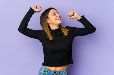 Mor arka planda izole edilmiş genç bir kadın özel bir günü kutluyor, atlıyor ve enerji ile kollarını kaldırıyor..