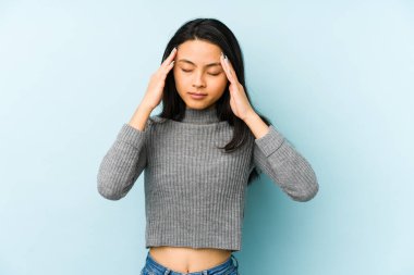 Mavi arka planda izole edilmiş genç Çinli kadın şakaklara dokunuyor ve baş ağrısı çekiyor..