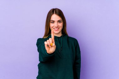 Mor arka planda izole genç beyaz kadın parmak ile bir numarayı gösteriyor..