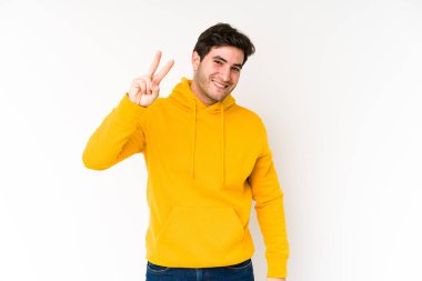Beyaz arka planda izole edilmiş genç adam neşeli ve kaygısız parmakları olan bir barış sembolü gösteriyor..