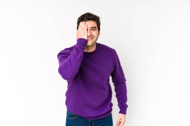 Beyaz arka planda izole edilmiş genç bir adam yüzünün yarısını avuç içiyle kaplayarak eğleniyor..