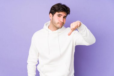 Mor arka planda izole edilmiş genç adam baş parmağını aşağı gösteriyor, hayal kırıklığı konsepti..