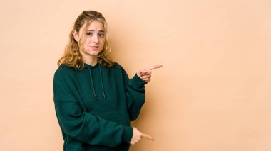 Beyazlı genç bir kadın bej arka planda izole edilmiş. İşaret parmaklarıyla bir fotokopi alanını işaret ederek şok olmuş..