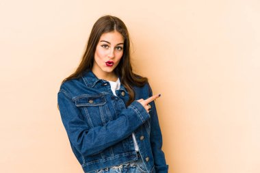 Beyaz tenli genç bir kadın bej arka planda izole edilmiş gülümsüyor ve boş alanda bir şeyler gösteriyor..