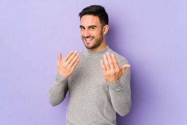Mor arka planda izole edilmiş genç beyaz adam sanki seni davet ediyormuş gibi seni işaret ediyor..
