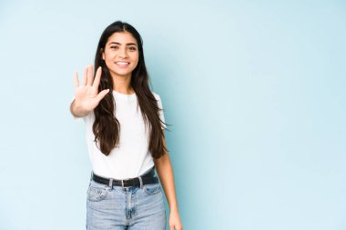Mavi arka planda gülümseyen genç Hintli kadın parmaklarıyla beş numarayı gösteriyor..
