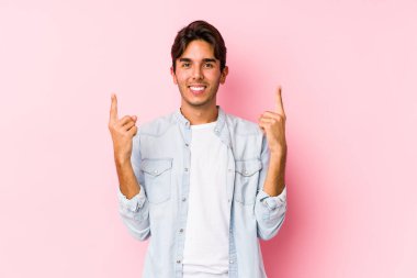 Pembe arka planda poz veren beyaz bir genç iki ön parmağı da boş bir alan gösteriyor..