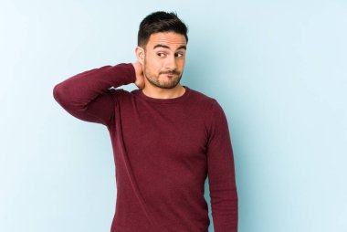 Kafkasyalı genç adam mavi arka planda izole edilmiş kafasının arkasına dokunuyor, düşünüyor ve bir seçim yapıyor..