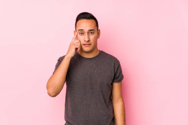 Yoong Latin adam pembe bir arka plan tapınağında poz veriyor. Parmağıyla düşünüyor, bir göreve odaklanıyor..