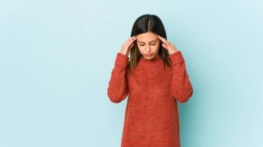 Mavi arka planda izole edilmiş genç bir kadın şakaklara dokunuyor ve başı ağrıyor..