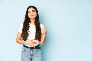 Mavi arka plandaki genç Hintli kadın karnına dokunuyor, nazikçe gülümsüyor, yemek yiyor ve tatmin oluyor..