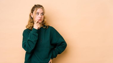 Beyazlı genç bir kadın bej arka planda izole edilmiş şüpheli ve şüpheci bir ifadeyle yana bakıyor..