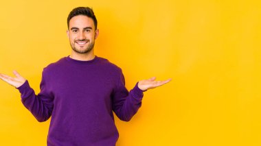 Sarı fırında izole genç beyaz adam kollarıyla ölçek yapar, mutlu ve kendinden emin hisseder..