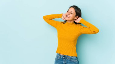 Mavi arka planda izole edilmiş genç bir kadın. Kollarını uzatıyor, rahat duruyor..