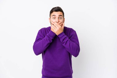 Beyaz arka planda beyaz tenli genç bir adam izole edilmiş. Elleriyle ağzını kapatan şok olmuş..