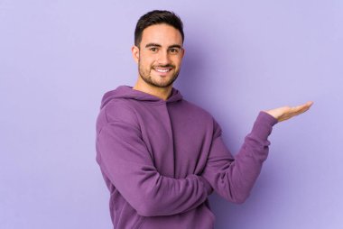 Mor arka planda izole edilmiş genç beyaz bir adam bir avuç içinde fotokopi alanı ve belinde bir el daha gösteriyor..