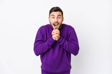 Beyaz arka planda yaşayan beyaz tenli genç bir adam şans için dua ediyor, şaşırıyor ve ağzını açıyor..