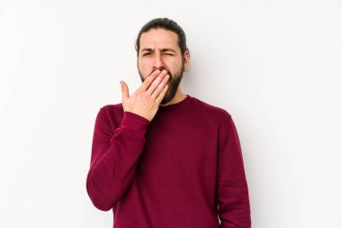 Genç, uzun saçlı adam beyaz bir arka planda izole edilmiş esniyor. Ağzı eliyle kapatan yorgun bir hareket sergiliyor..