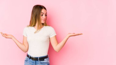 Pembe arka planda soyutlanmış beyaz bir kadın. Kafası karışmış ve omuz silkiyor. Kopya alanını tutmak için..