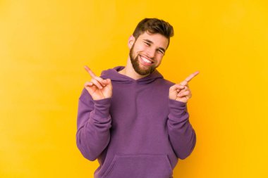 Sarı arka planda izole edilmiş genç beyaz adam farklı kopya alanlarını gösteriyor, birini seçiyor, parmağıyla gösteriyor..