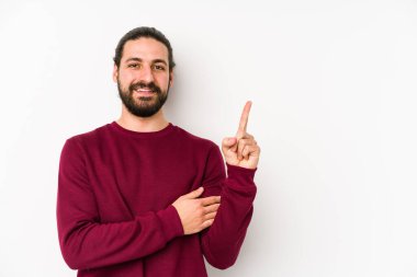 Genç, uzun saçlı adam, beyaz bir arka planda izole edilmiş. Gülümsüyor, işaret parmağıyla işaret ediyor..
