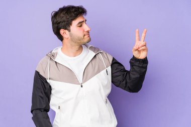 Mor arka planda izole edilmiş genç adam neşeli ve kaygısız parmakları olan bir barış sembolü gösteriyor..
