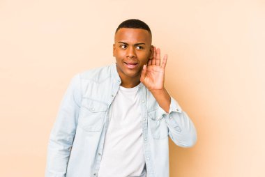 Genç Latin bir adam bej arka planda izole edilmiş bir şekilde bir dedikoduyu dinlemeye çalışıyor..