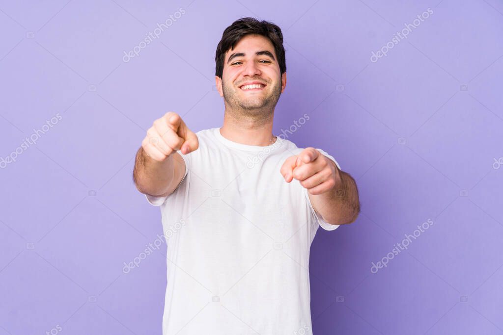 Young man isolated on purple background cheerful smiles pointing to front.