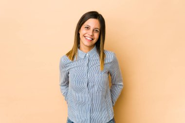 Bej arka planda izole edilmiş genç bir kadın mutlu, güler yüzlü ve neşeli.