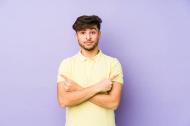 Mor arka plan noktalarında izole edilmiş genç bir Arap, iki seçenek arasında seçim yapmaya çalışıyor..