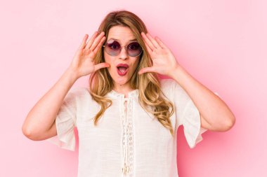 Pembe arka planda gözlüklü genç beyaz kadın hoş bir sürprizle karşılaşıyor, heyecanlı ve el kaldırıyor..