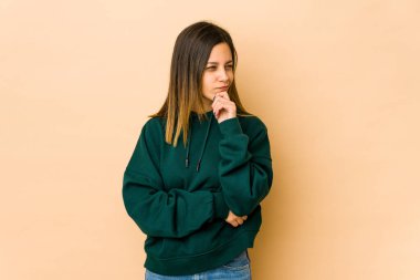 Bej arka planda izole edilmiş genç bir kadın düşünüyor, yukarı bakıyor, yansıtıyor, düşünüyor, fantezi kuruyor..